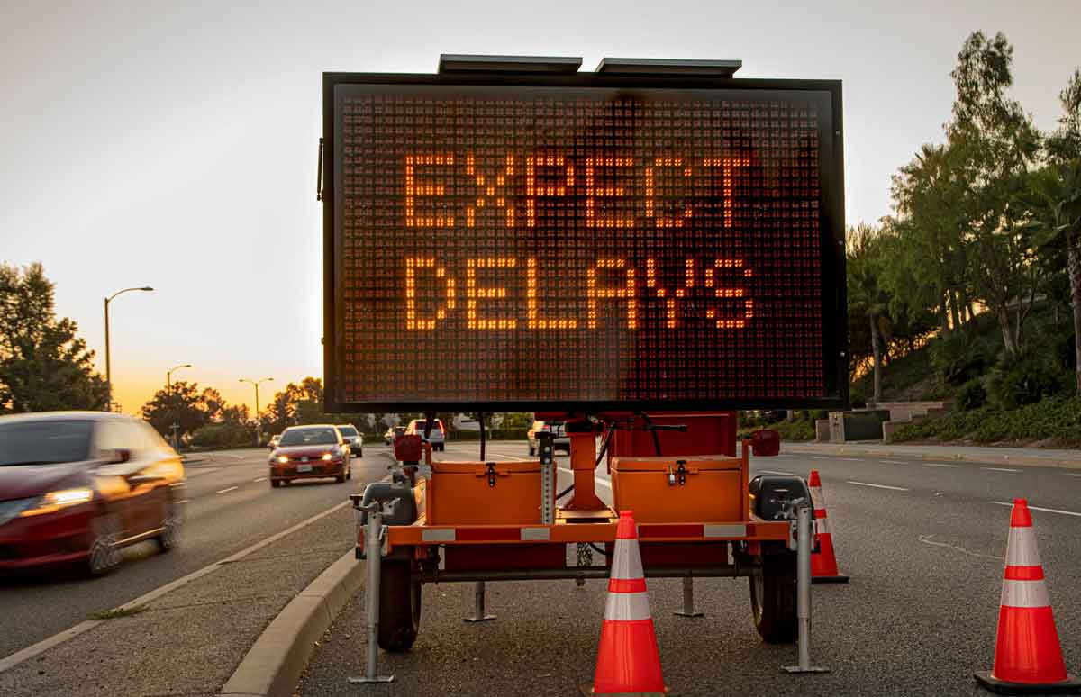 Traffic control sign displaying the words 'Expect Delays’ as cars drive by